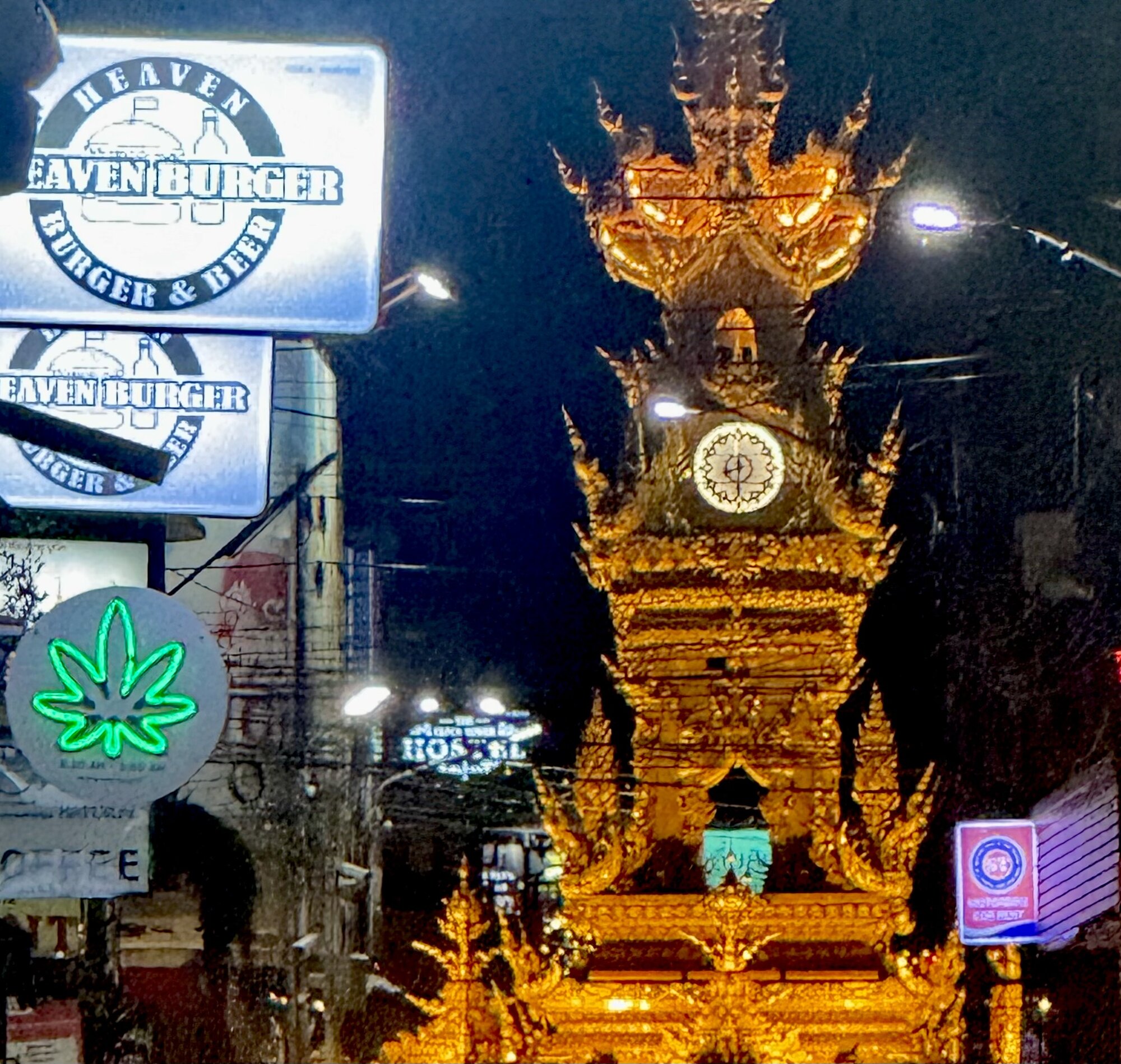 A cannabis dispensary sign lit up beside Chiang Rai's clock tower at night.